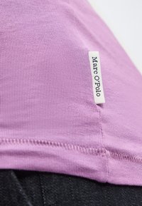 Gros plan sur un tissu violet côtelé avec des coutures visibles et une étiquette blanche de vêtement portant l'inscription "Marc O'Polo".