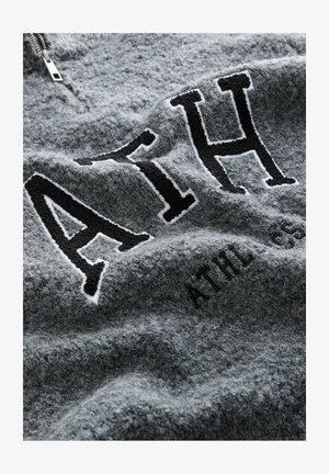 Grijze fleece pullover met een halve rits, voorzien van zwarte geborduurde letters "ATH" en een subtiele textuur. Zacht, comfortabel materiaal met een licht versleten uitstraling.