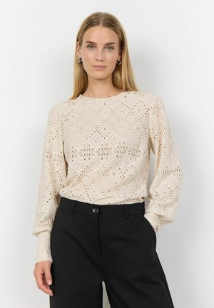Beige dlouhý rukáv top s květinovou výšivkou a otvorovým detailem; spárováno s černými kalhotami s vysokým pasem.