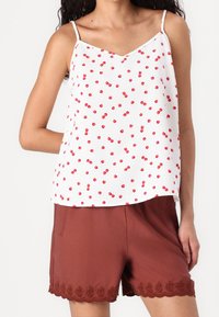 Débardeur blanc avec motif de cerises rouges, décolleté en V et fines bretelles, associé à un short marron avec un fin bord en dentelle festonnée.