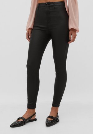 Czarne spodnie dżinsowe z wysokim stanem, wykonane z elastycznego materiału, o slim fit i subtelnym przeszyciu. Połączone z czarnymi balerinami z noskiem w szpic, ozdobionymi ćwiekami.