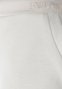 Lysebeige joggingbukser lavet af blødt stof med en glat tekstur, elastisk talje og diskret "BWLDR" broderi.