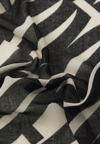 Schwarz-weißer Stoff mit einem Muster aus abstrakten Zickzackformen. Das Material wirkt leicht und luftig mit einer strukturierten Oberfläche.