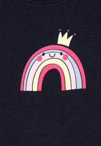 T-shirt bleu marine avec un graphique arc-en-ciel multicolore représentant un visage souriant surmonté d'une petite couronne. Texture de tissu lisse.