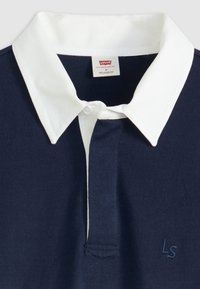 Polo de color marino con cuello blanco, tejido suave, tapeta de tres botones, bordado "LS" en el pecho y diseño de corte relajado.