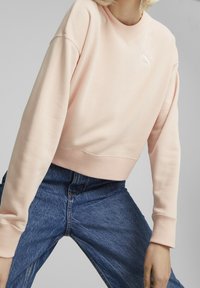 Felpa cortata rosa con collo rotondo, polsini a coste e logo ricamato. Abbinata a jeans in denim per un look casual.