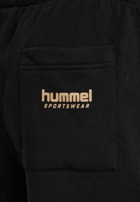 Zwarte joggingbroek met een zachte textuur, voorzien van een klein, gouden "hummel SPORTSWEAR" logo en een achterzak met gekleurde stiksels.