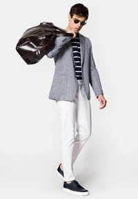 Dopasowana niebieska marynarka w kostkę, pasiaste granatowo-białe koszula, białe spodnie, granatowe trampki i ciemnobrązowa skórzana torba.