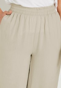 Light beige, loose-fitting pants with an elastic waistband and side pockets, made of crinkled fabric, providing a textured appearance.