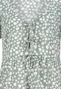 Blumenkleid aus hellgrünem Stoff, mit V-Ausschnitt, kurzen Ärmeln und einem schwingenden Rock. Weiße Blumen mit rosa Akzenten überall.