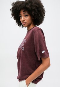 Burgundijas oversize t-krekls, kas izgatavots no mīkstas kokvilnas, ar īsām piedurknēm. Priekšpusē ir balts "NIKE"logs un mazs logo uz piedurknes.