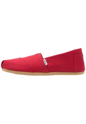 Scarpa slip-on in tela rossa con punta arrotondata e inserti elastici ai lati. Presenta una suola in gomma marrone e un piccolo etichetta di marca vicino al tallone.
