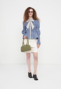 Μπλούζα μπλε και λευκή με καρό μοτίβο, μανίκια φουσκωτά και δετή γιακά, σε συνδυασμό με λευκή φούστα και πράσινη τσάντα. Μαύρα παπούτσια με τακούνι.