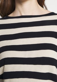 Sweter z prążkowanego materiału w na przemian niebieskie i beżowe poziome paski, okrągły dekolt i gładka faktura. Brak dodatkowych szczegółów.