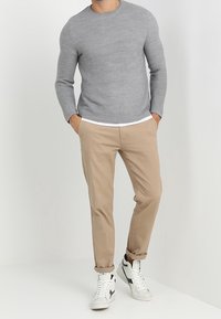 Golf grigio a maniche lunghe con collo rotondo, dal tessuto a costine, abbinato a pantaloni chinos beige e sneakers bianche alte con dettagli neri.