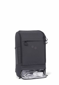 Schwarzer Stoff-Rucksack mit einer zipfähnigen Fronttasche, runden Hardware-Akzenten und einem unteren Fach, das ein weißes Ladekabel und einen Adapter enthält.