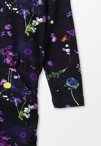 Svart tyg med ett blommönster i lila, rosa, grönt och vitt, förstärkt med en blå ros och utspridda färgglada cirklar.