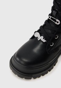 Μαύρο δερμάτινο μποτάκι με παχύ πάτο, μαύρες γειτώδες και διακοσμητικές ασημένιες πέρλες ασφαλείας με ρουμπίνι προσδεδεμένες σε αυτές.