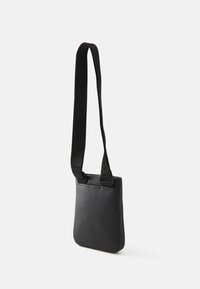 Black leather crossbody bag with a rectangular shape, adjustable textile strap, and minimalist design. Smooth texture with minimal accents.