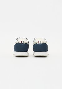 Sneaker con una toma in suede blu scuro e accenti color crema. Presenta una suola bianca e un dettaglio a strisce rosso, bianco e blu sul tallone.