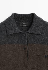 Maglione polo in cashmere con una sezione superiore grigio scuro, una sezione inferiore marrone, colletto a costine, due bottoni e una tasca sul lato sinistro.