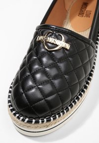 Mocassin noir en cuir matelassé avec logo en métal doré. Caractérisé par une bordure en jute tressé contrastante et une doublure intérieure lisse.