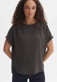 Top nero a maniche corte, caratterizzato da un motivo geometrico di piccoli triangoli in beige e blu. Vestibilità ampia con scollatura tonda.