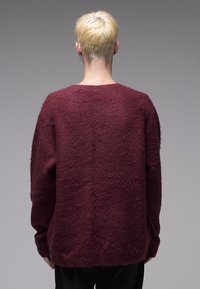 Μπορντό πλεκτό πουλόβερ με αφράτη υφή, άνετη εφαρμογή και φαρδιά στρογγυλή λαιμόκοψη. Διαθέτει μακριά μανίκια και ίσια τελείωμα στο πίσω μέρος.