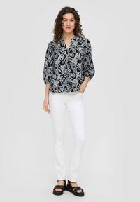 Zwart-witte blouse met paisleypatroon, lichtgewicht stof, v-hals, driekwart mouwen, gecombineerd met witte slim-fit broeken en zwarte sandalen.