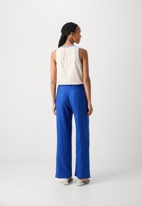 Loose-fitting white sleeveless top with textured fabric paired with bright blue wide-leg pants. Simple design with no visible patterns, smooth finish.