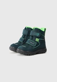 Ciemnozielone buty z neonowozielonym wykończeniem, posiadające dwa paski na rzepy i teksturowane czarne gumowe podeszwy, zaprojektowane do użytku na zewnątrz.
