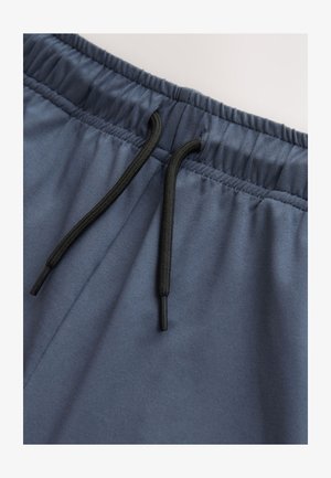 Temnomodre športne kratke hlače z elastičnim pasom, z črnim vrvico za zategovanje in gladko teksturo. Povečani posnetek prikazuje podrobnosti pasu.