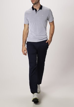 Jasnoniebieska koszulka polo z czarnym kołnierzykiem i małym logo, zestawiona z granatowymi spodniami i białymi sneakersami z żółtymi akcentami.