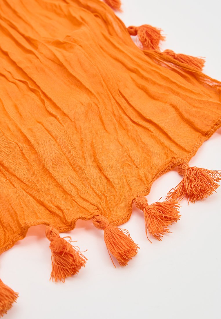 Jasnopomarańczowa tkanina z miękkimi zmarszczkami i frędzlami po jednej krawędzi na białym tle.