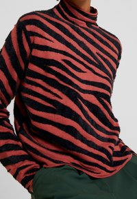 Maglione a maniche lunghe con colletto alto in corallo con strisce verticali nere. Tessuto morbido e strutturato con una vestibilità rilassata e un collo alto.