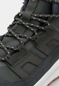 Scarpa nera con tomaia testurizzata, lacci spessi con dettagli chiari e una suola intermedia bianca a contrasto. Include una suola in gomma per la trazione.