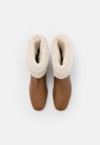 Bottes en cuir marron avec un poignet en shearling crème doux. Le design présente un bout rond et des détails de couture verticaux.