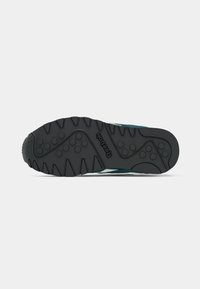 Crni gumeni potplat Reebok tenisice s kružnim uzorcima za prianjanje i detaljima u obliku zigzaga na bijeloj pozadini.