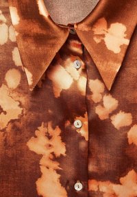 Camicia tie-dye marrone e beige con colletto a punta e tre bottoni in perla visibili sul davanti.