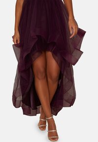 Burgundin tüllimekko, jossa on nyörityksellä varustettu korkeampi ja matalampi helma, läpikuultava pinta, ja asusteena metallinhohtoiset kiilakorkokengät.