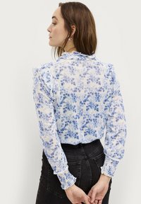 Blumenbluse aus leichtem, durchsichtigem Stoff mit blauen Blumenmustern, Rüschensaum am Hals und smockierten Manschetten.