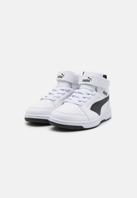 Baskets montantes en cuir blanc avec une bande latérale noire, un col rembourré et une sangle velcro. Comprend des perforations pour la respirabilité.