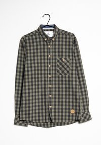 Camisa abotonada de cuadros verdes y negros con mangas largas, bolsillo en el pecho, botones de madera y una parche con logotipo en el dobladillo.