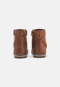 Bottines en daim marron avec une finition texturée, une fermeture éclair et un panneau contrastant sur le côté. Semelle en caoutchouc plate.