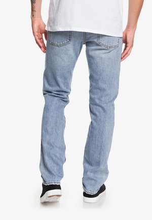 Jeans de mezclilla azul claro con corte recto, que cuentan con bolsillos traseros, costuras en contraste y una ligera textura de desvanecimiento. Llevados con zapatos negros.