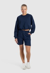 Felpa blu navy corta con cintura elastica e pantaloni shorts abbinati. Presenta una vestibilità comoda, tessuto morbido e tasche laterali.