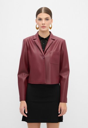 Veste cropped en simili cuir bordeaux avec une fermeture à un bouton, des revers en pointe et une poche poitrine, portée sur un top en dentelle noir.