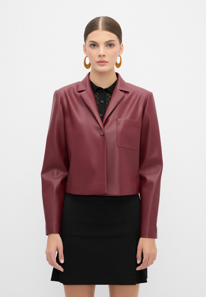 Bordeaux faux læder cropped jakke med en enkelt knaplukning, udsnit lapeller og en brystlomme, båret over en sort blonde top.