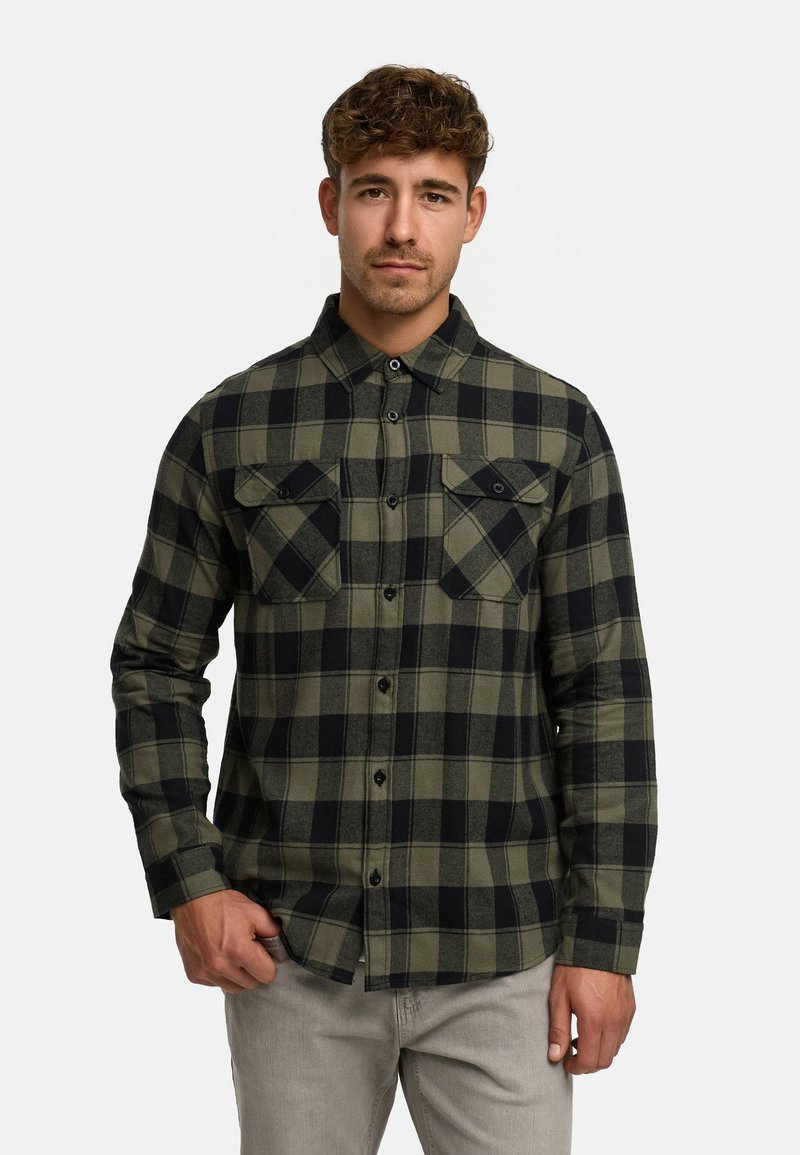 Camisa de franela a cuadros verdes y negros, con mangas largas, cierre de botones en el frente y dos bolsillos en el pecho. Textura suave con un ajuste clásico.