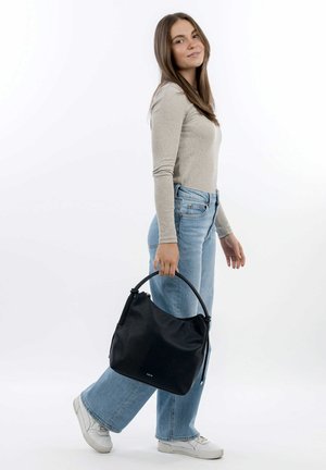 Black leather hobo bag with a textured surface, zip closure, and a round handle, held by a person wearing light blue jeans and white sneakers.